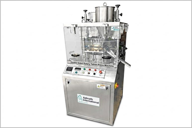 Stainless steel double-sided rotary tablet press machine with a transparent safety enclosure and control panel on the front.