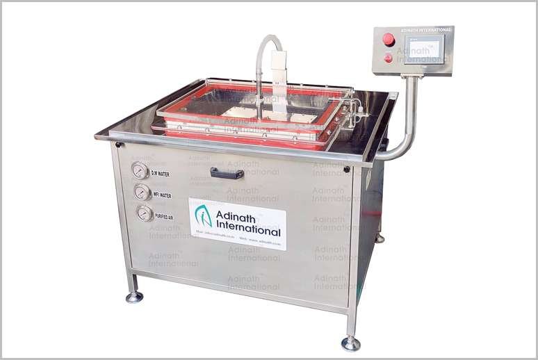 Stainless steel ultrasonic cleaning bath with a transparent lid and control panel on the side, labeled Adinath International