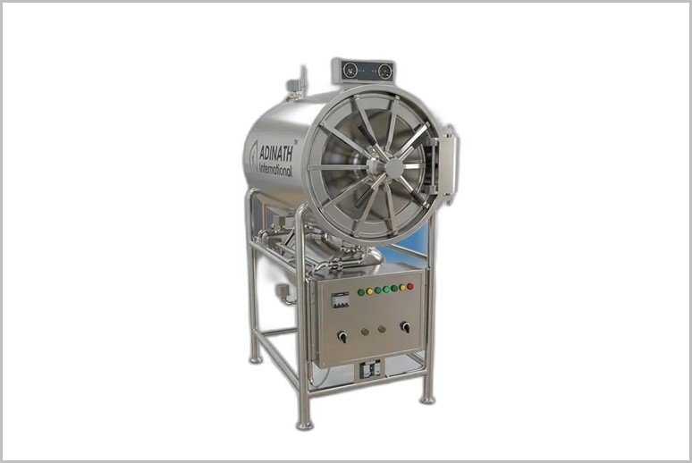 Industrial stainless steel autoclave on a frame with a large circular door and control panel, branded Adinath International, used for sterilization.
