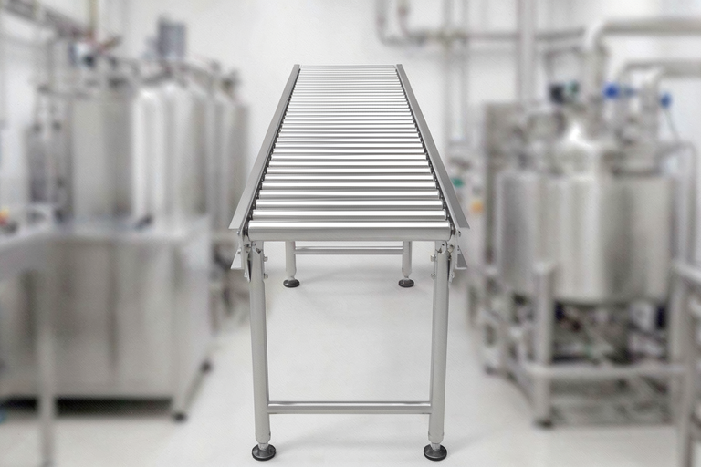 Stainless steel roller conveyor in a clean industrial facility, with large stainless tanks in the background.