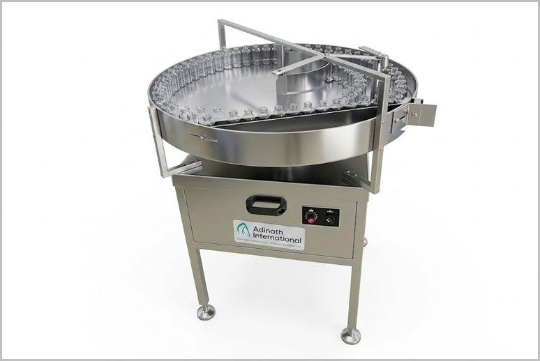 Industrial stainless steel rotary bottle conveyor with a circular track and glass bottles on a bottling line