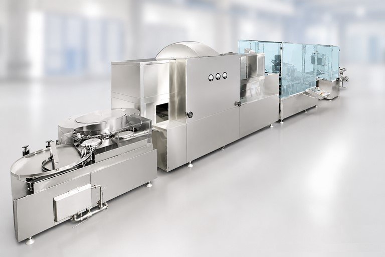 Industrial stainless-steel food-processing production line in a clean, bright facility with glass guards on the right segment of the machine
